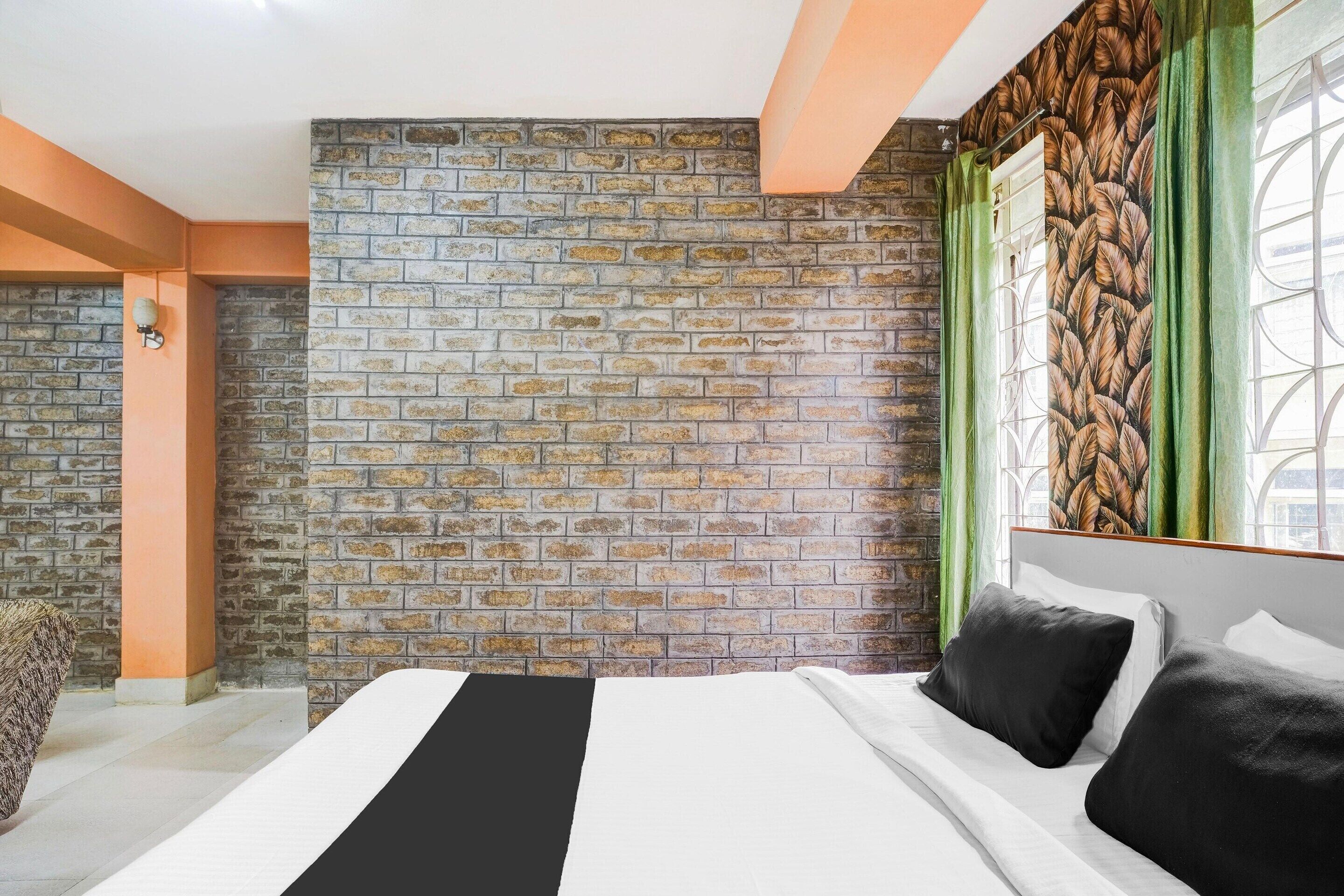 A bedroom with a brick-patterned wall, a bed with white and black bedding, and a window with green curtains.