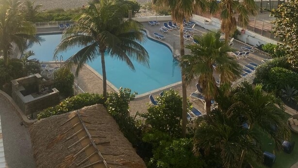A resort with a pool, palm trees, and a view of the beach.
