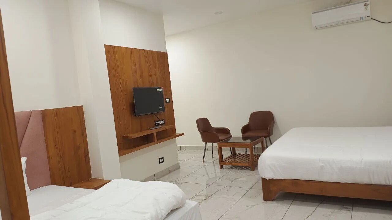 Une chambre d’hôtel avec deux lits simples, un meuble en bois pour la télévision, une petite table avec deux chaises et un appareil de climatisation blanc.