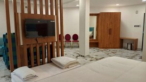 A hotel room with a bed, a TV mounted on a wooden partition, a wardrobe, and two red chairs. - Tej Hotel & Restaurant  (Tikamgarh)