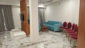 A living room with a sofa, chairs, a TV, and a wooden partition. - Tej Hotel & Restaurant  (Tikamgarh)