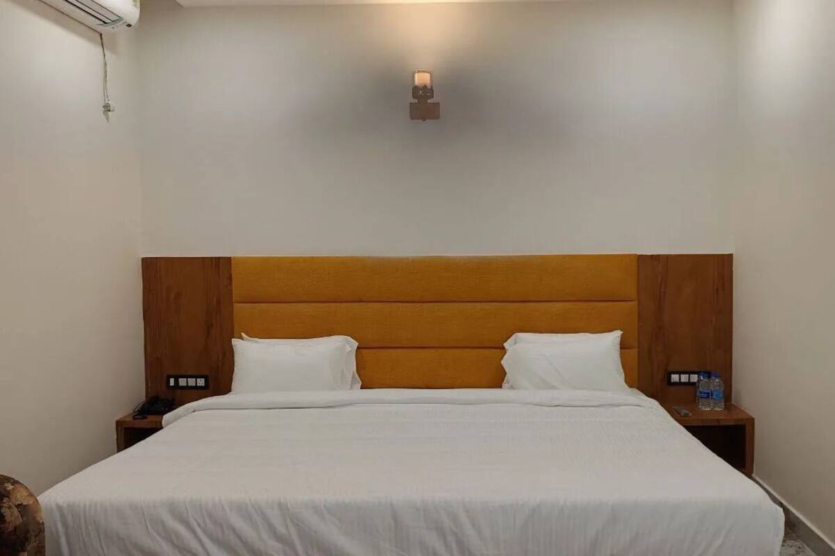 Una cama bien hecha con cabecera de madera, dos mesitas de noche con lámparas y un aplique en la pared.