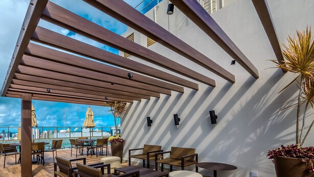Un área de estar exterior con mobiliario de madera, una pérgola y plantas en macetas.