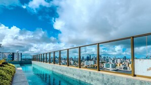 Una piscina en la azotea con vista a la ciudad, amplios ventanales de vidrio y suelo de baldosas.