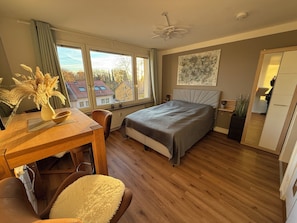 A bedroom with a bed, a desk, a chair, a radiator, a window, and a ceiling fan.