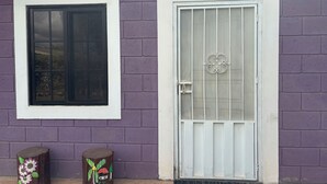 A house with a purple brick exterior, a white door with a metal gate, and a window with a black frame. - Charming 2-bedroom apartment with WiFi in Intibuca (Intibuca)