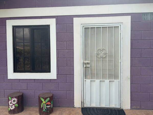 A house with a purple brick exterior, a white door with a metal gate, and a window with a black frame.