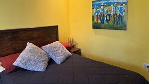 A bedroom with a large bed, two fluffy pillows, a wooden headboard, a painting on the wall, and a bedside table with a lamp. - Charming 2-bedroom apartment with WiFi in Intibuca (Intibuca)