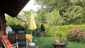 An outdoor patio with white rocking chairs, a yellow umbrella, and a barbecue grill.
