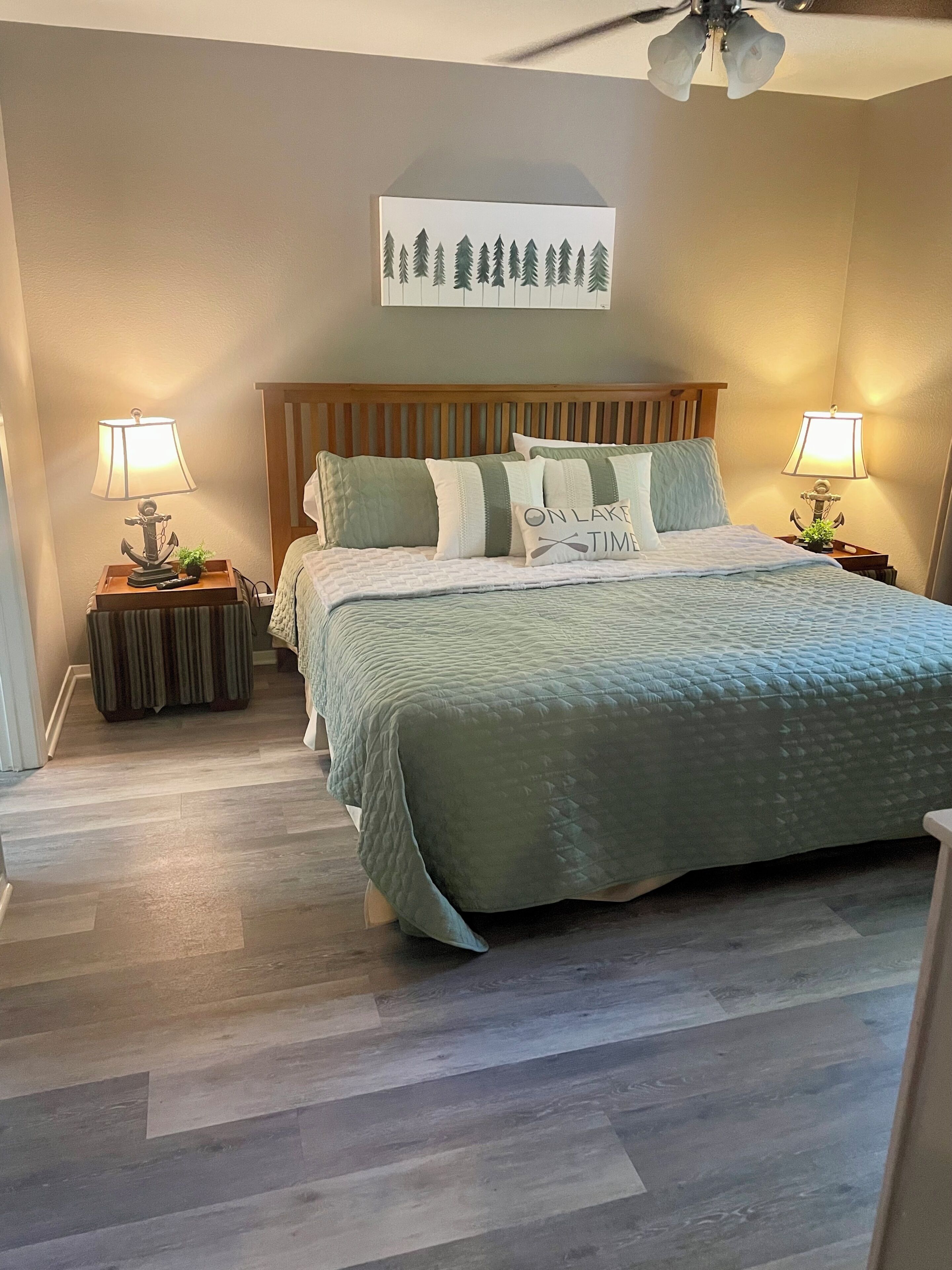 A bedroom with a bed, two nightstands, a ceiling fan, and a wall-mounted painting.