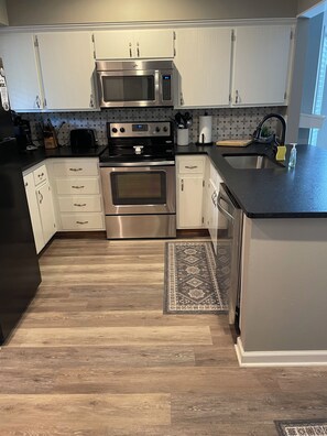 A modern kitchen with stainless steel appliances, white cabinetry, and a wooden floor.