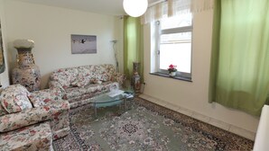 A living room with a floral sofa, a glass coffee table, a large vase, and a patterned rug.