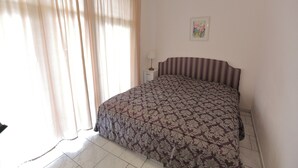 A bedroom with a bed, curtains, a nightstand, a lamp, and a framed picture on the wall.