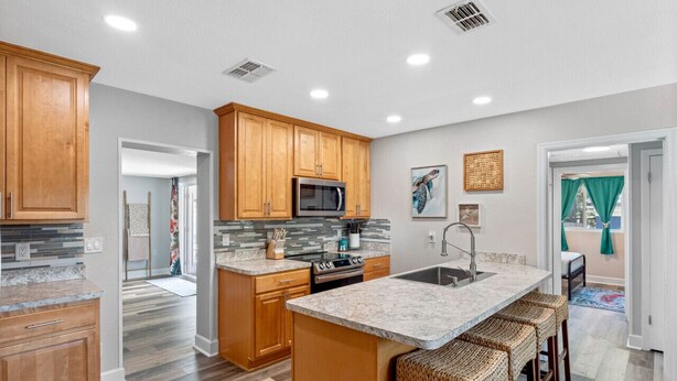 A modern kitchen with wooden cabinets, a central island with bar stools, a stainless steel refrigerator, and a microwave. - Charming 3-Bedroom, 2-Bathroom Home with Heated Pool and Spacious Backyard in the Heart of Lakeland (Lakeland)