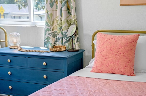 A bedroom with a blue dresser, a pink bedspread, and a matching pillow.