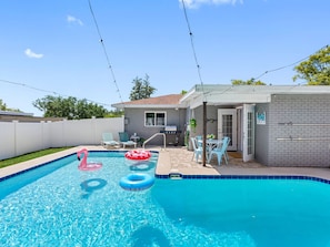 A swimming pool with two inflatable rings, a barbecue area, and a patio with chairs. - Heated Pool Home Near Theme Parks | 3BR, Sleeps 7, Fenced Yard, Shops Across the Street (Lakeland)