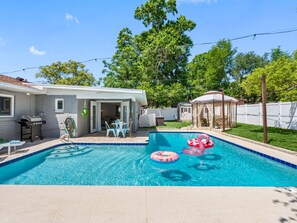 A backyard with a swimming pool, inflatable flamingos, and a covered patio area.