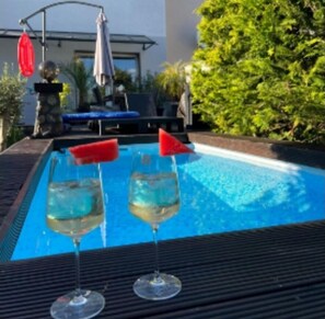A swimming pool with two glasses of a clear liquid, possibly a cocktail, on a table. - Beautiful apartment, on the first floor of my own home, with garden access and pool (Zörbig)