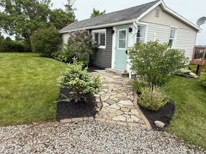 A house with a stone pathway leading to the door, surrounded by a well-maintained lawn and various plants. - Ocean view house (Overton)