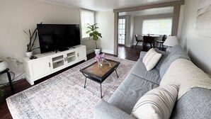 A living room with a large flat-screen TV, a sofa, a coffee table, and a dining area in the background. - Ocean view house (Overton)
