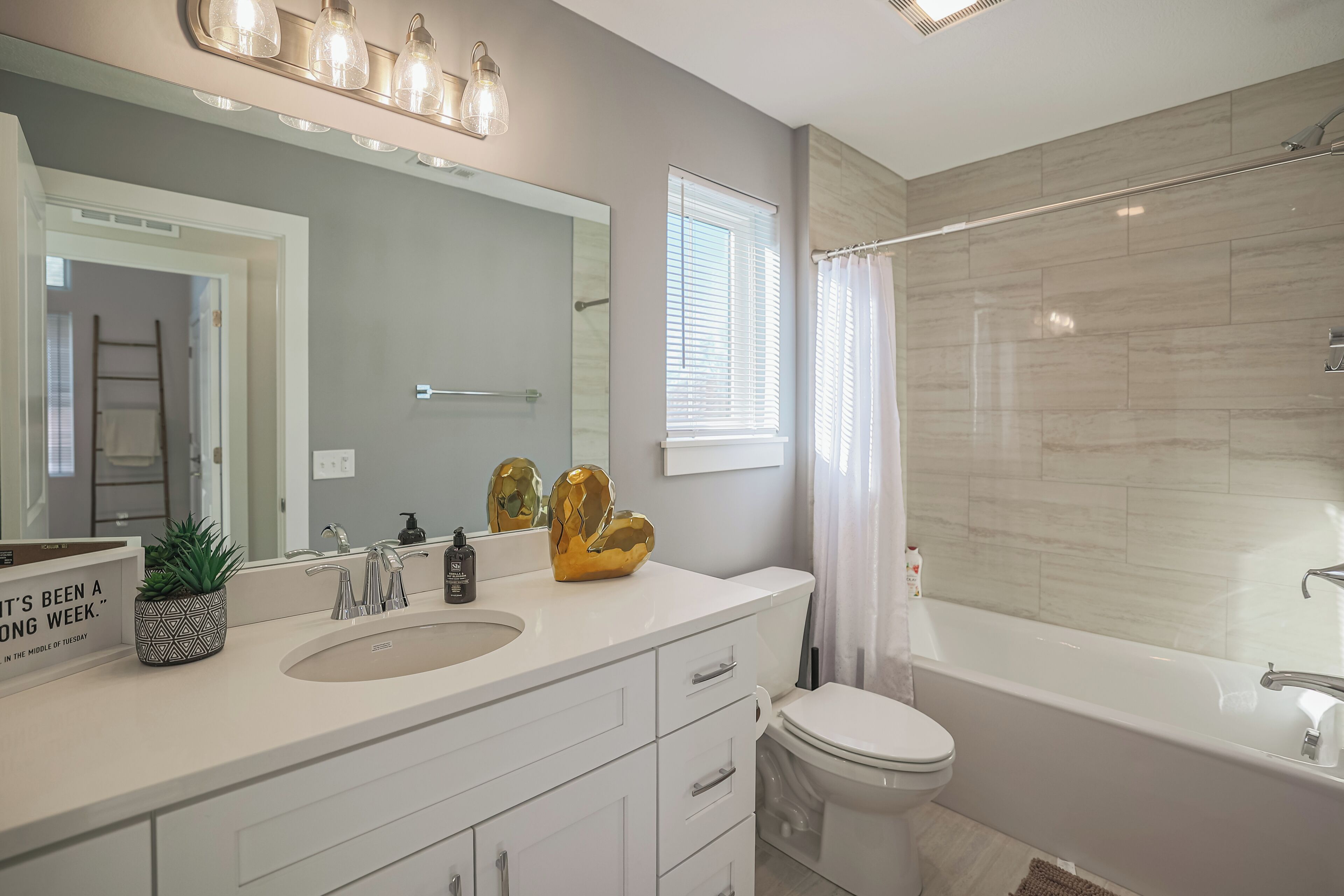 A modern bathroom with a white sink, vanity, and toilet, a large mirror, and a walk-in shower.