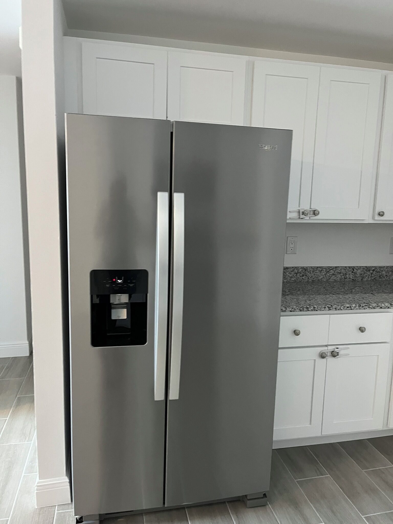 A stainless steel refrigerator with a water dispenser, white cabinets, and a granite countertop. - Cozy Lehigh Extended Stay (Lehigh Acres)