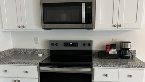 A kitchen with white cabinets, a stainless steel microwave, an oven, and a coffee maker. - Cozy Lehigh Extended Stay (Lehigh Acres)
