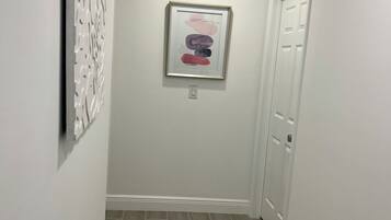 Un pasillo con un cuadro abstracto enmarcado en la pared, una puerta al final y una lámpara en el techo.