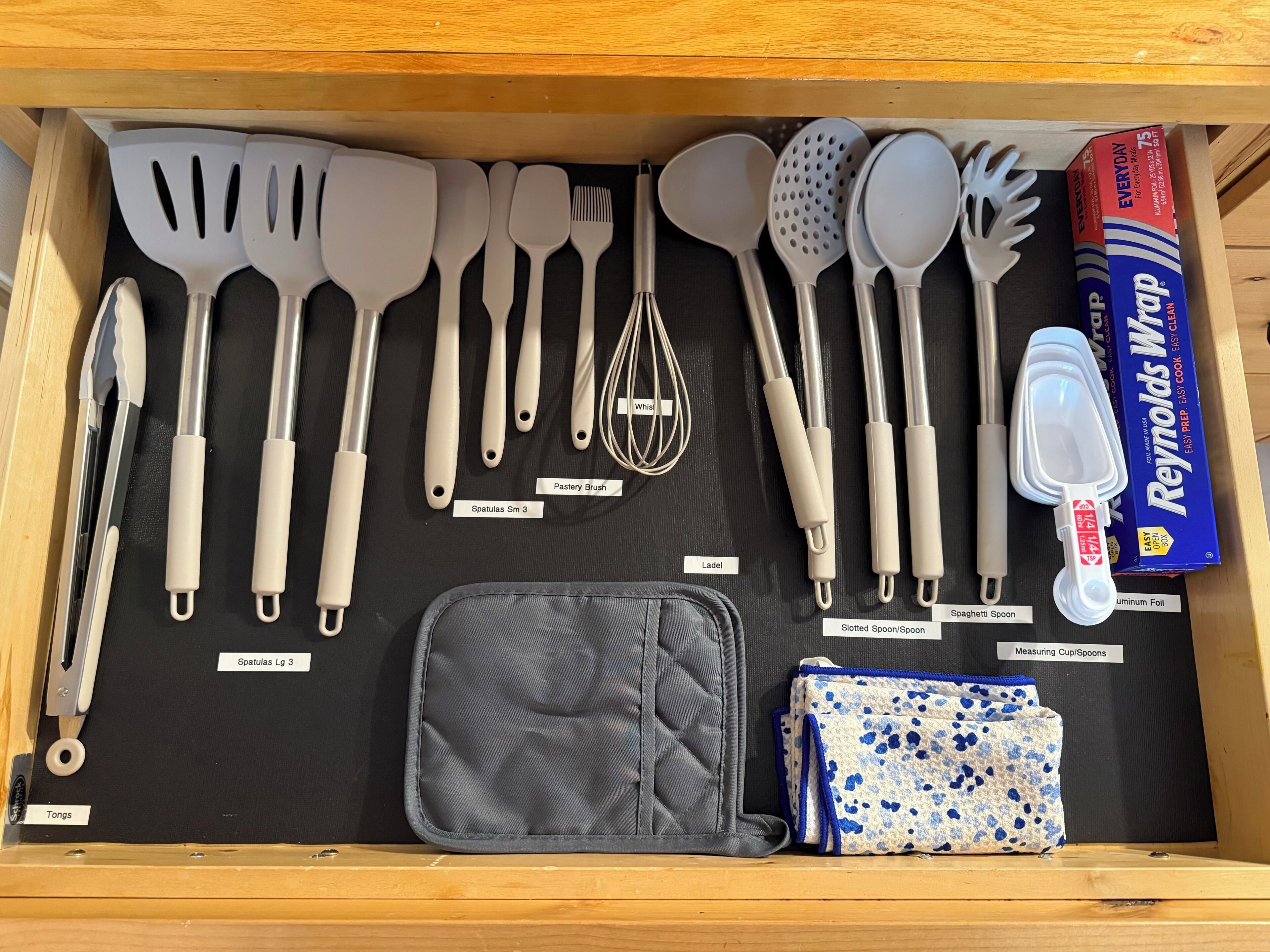Un cajón con diversos utensilios de cocina y una caja de papel de aluminio Reynolds Wrap.
