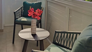 Una habitación iluminada por el sol con vistas al mar, con dos sillas, una mesita y un jarrón con flores.