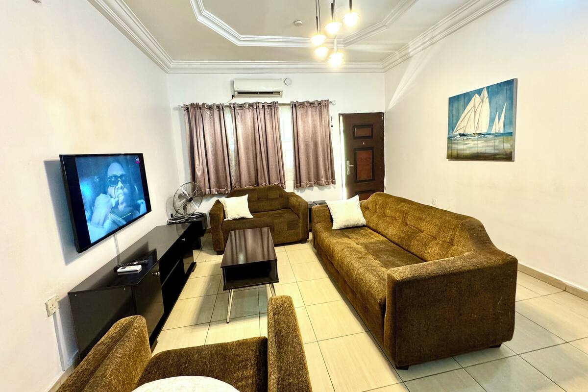 A living room with a sofa set, a TV, a fan, and a painting on the wall.