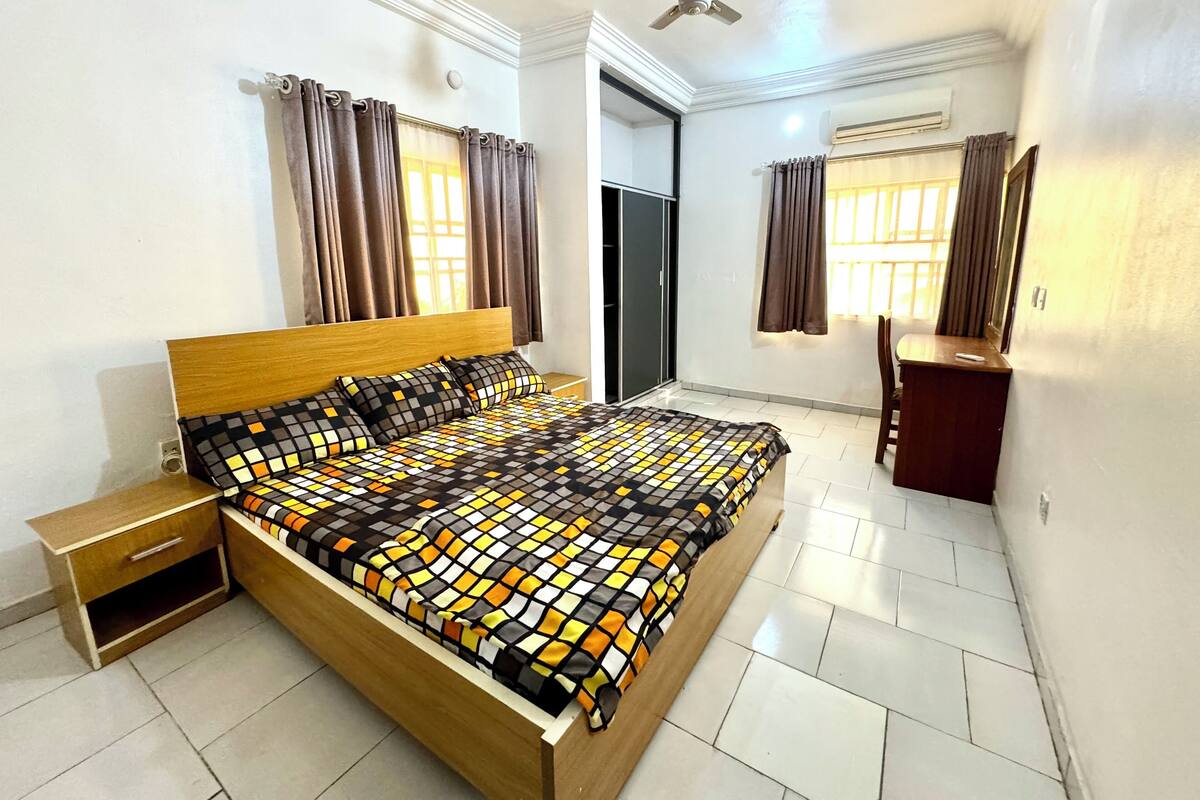 A bedroom with a wooden bed, a nightstand, a desk, and a chair.
