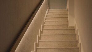 A carpeted staircase with a handrail on the left and a light source at the top. - Alumaro House (Castellammare del Golfo)