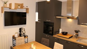 A modern kitchen with a flat-screen TV, built-in oven, and a wooden dining table. - Alumaro House (Castellammare del Golfo)