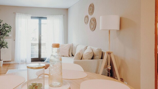 Una sala de estar moderna con un sofá, una mesa con adornos, una lámpara y vistas a través de un ventanal.