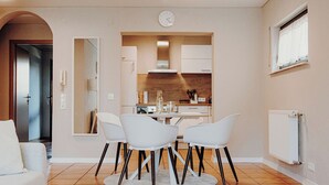 Una cocina moderna con armarios blancos, una mesa redonda de comedor con cuatro sillas y un reloj visible en la pared.