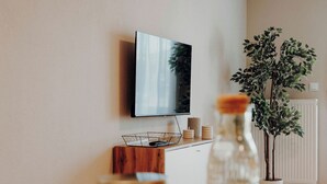 Una sala de estar moderna con un televisor de pantalla plana montado en la pared, un aparador de madera, una planta en maceta y una botella de vidrio sobre una mesa.