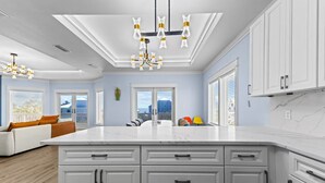 A modern kitchen with white cabinets, a marble countertop, and a central island. - Ocean View, Modern, Elegant Oasis With Private Pool In Gated, Coastal Community! (Eastpoint)