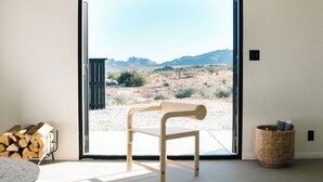 Una habitación con una silla de madera cerca de un ventanal corredizo, una pila de leña y una cesta tejida.