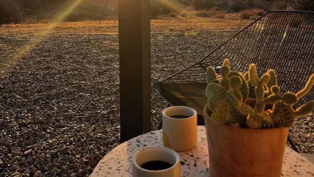 Una terraza con vistas a la puesta de sol, una planta de cactus y dos tazas de café sobre una mesa.