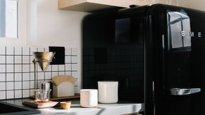 Una cocina moderna con un refrigerador negro, estantes de madera y una cafetera.