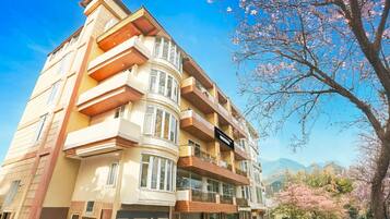 Un edificio de varios pisos con balcones, una señal que indica que es un hotel y flores de cerezo al fondo.