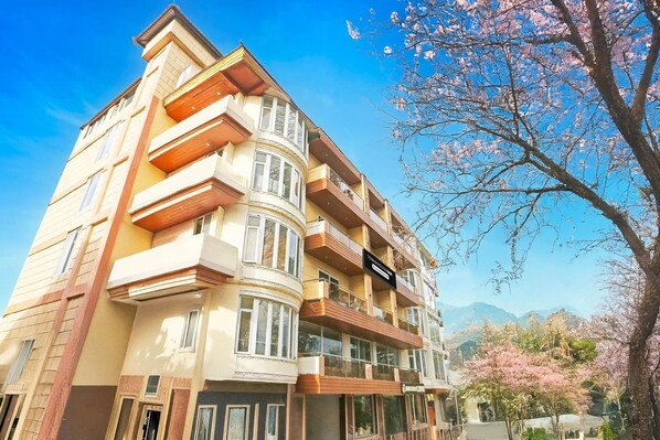Un edificio de varios pisos con balcones, una señal que indica que es un hotel y flores de cerezo al fondo.