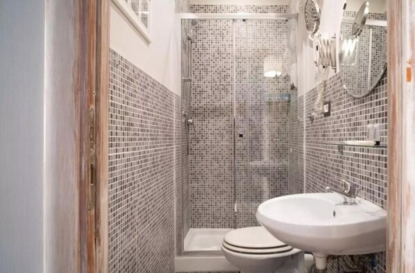 A bathroom with a shower, toilet, and sink, featuring mosaic tile walls and a wooden door frame. - Domus Ferruccio (Rome)