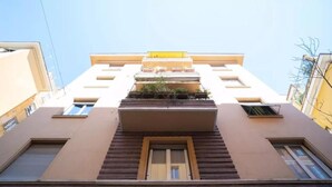 Ein mehrstöckiges Gebäude mit einem zentralen Balkon, Fenstern und einem gelben Markisenvorbau.