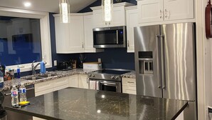 Een moderne keuken met witte kasten, roestvrijstalen apparatuur, een centraal eiland met krukken en hanglampen.