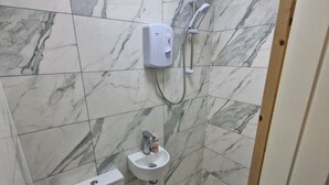 Un baño con inodoro, lavamanos, ducha y extractor.