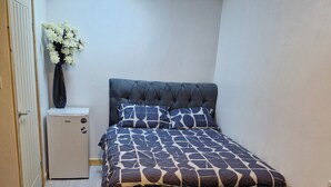 Un dormitorio con una cama, un mueble blanco pequeño, un florero con flores y suelo de madera.