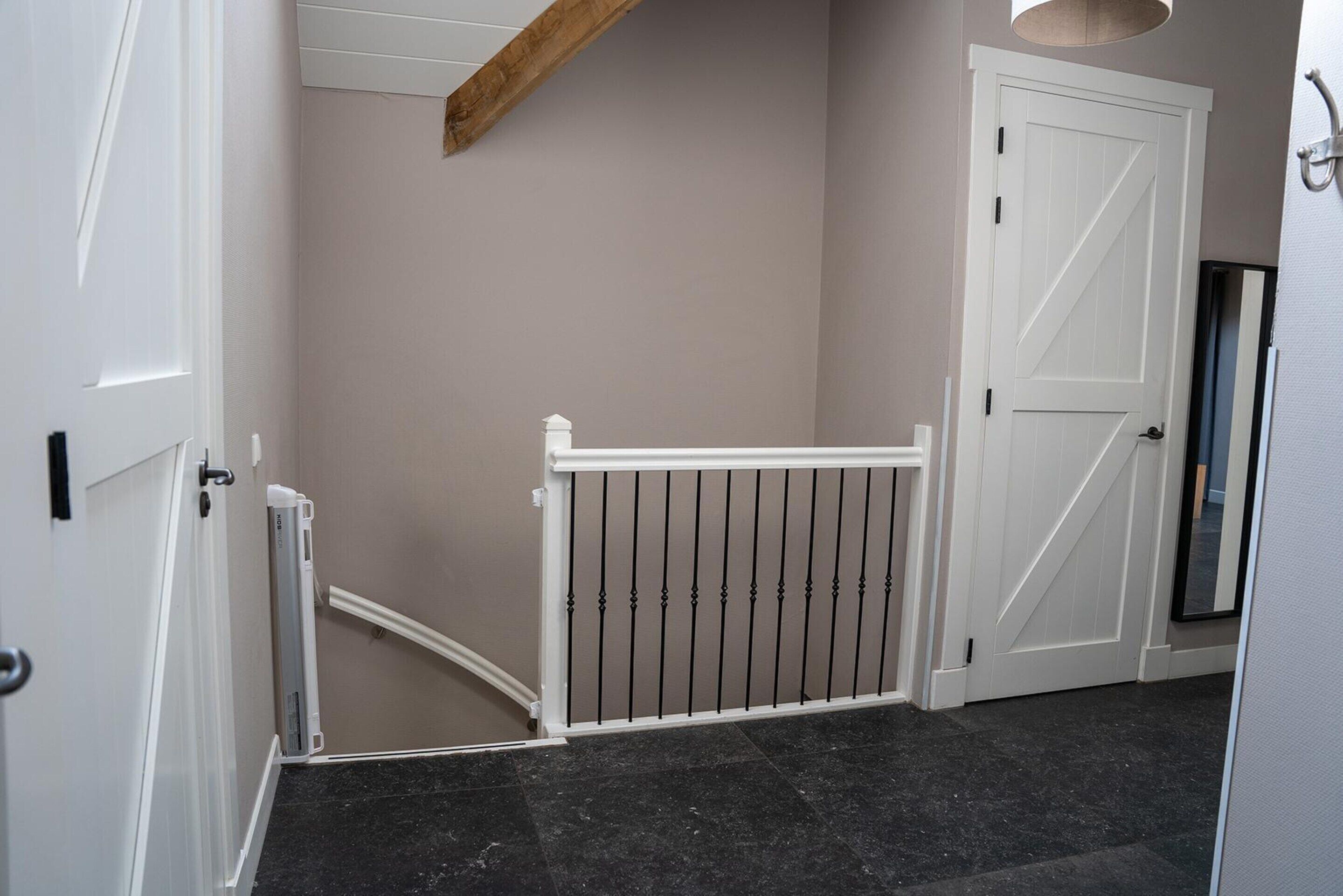 A hallway with a white door, a white railing, and a black tiled floor.
