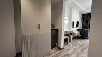 Una camera d'albergo moderna con pavimento in legno, un armadio dalle linee verticali, una scrivania con una sedia, un divano e una televisione a parete.
